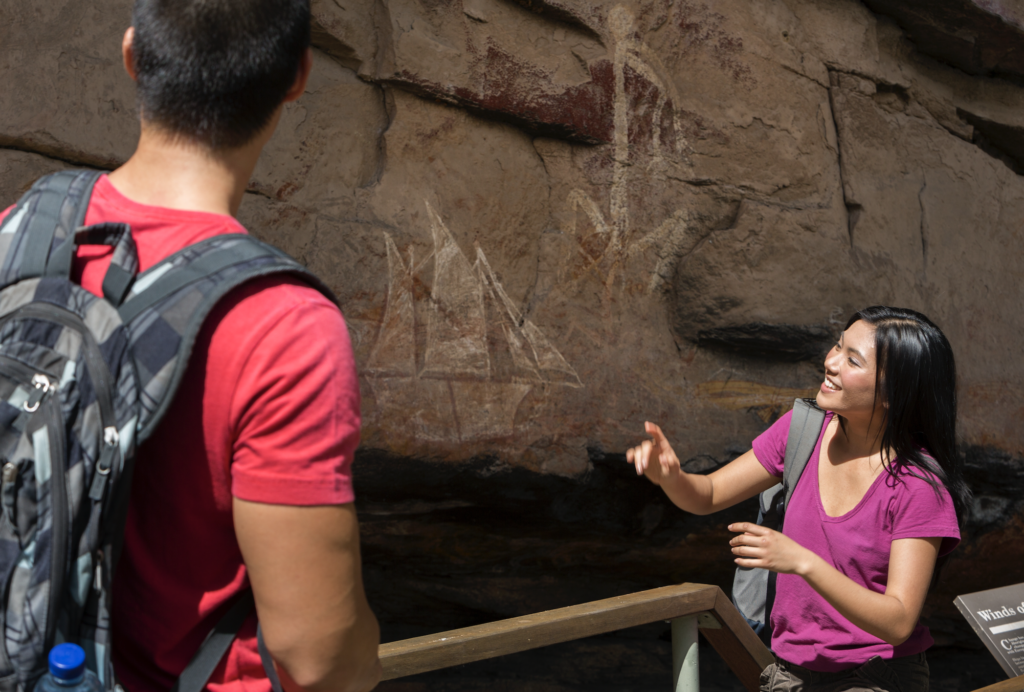 two people observe the rock art at Burrungkuy/Nourlangie Rock. The rock art depicts a European sailing ship. 