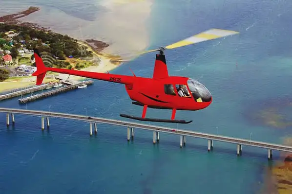 A red tour helicopter in flight over Phillip Island