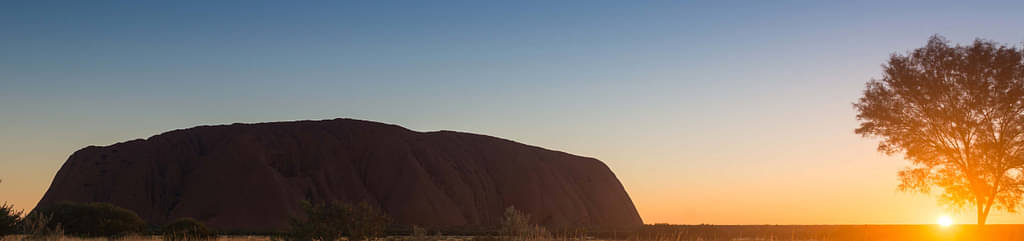 Sun On The Horizon Behind The Uluru Rock