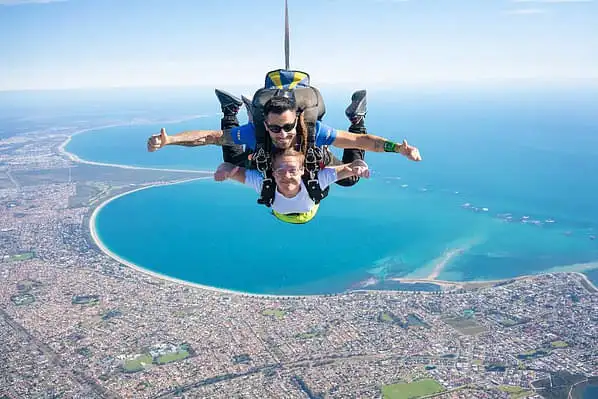 A photo of a skydiver free falling over the city of Perth and the ocean beyond.