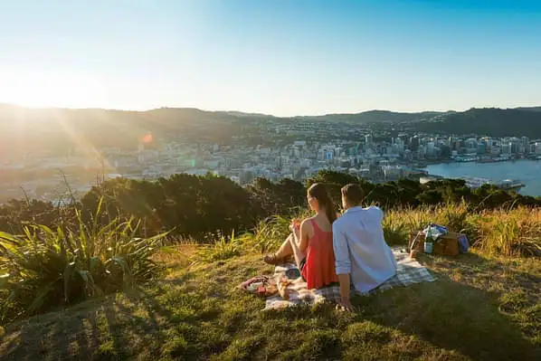 Two people relaxing at the summit on Tangi Te Keo (Mount Victoria) and looking out at Wellington city below. 
