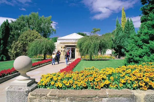 The entry to the Royal Tasmanian Botanical Gardens lined with red and yellow flowers, pristine lawns, and lush trees