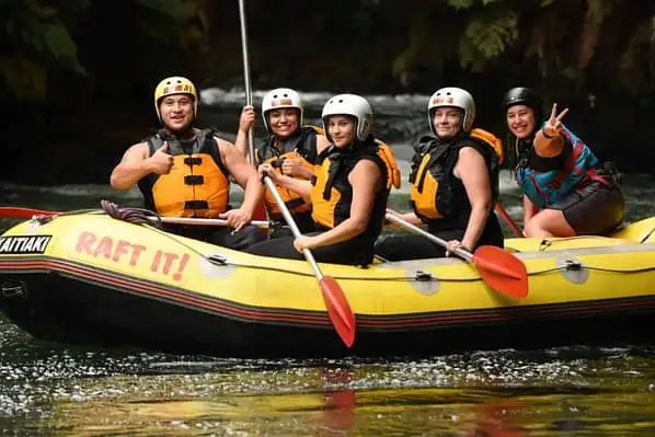 A group of people in a single rafting boat paddling along a calm river.