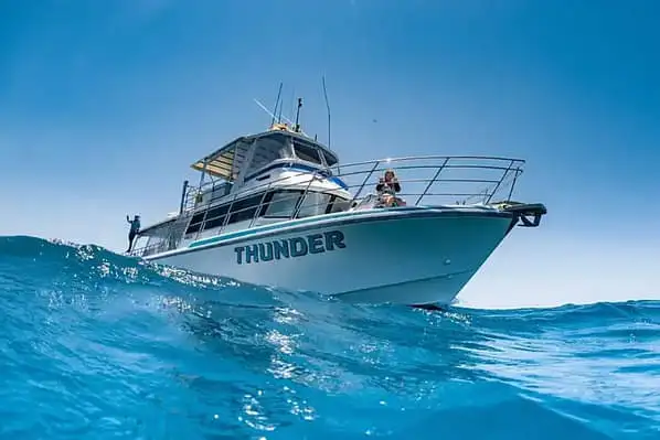 A photo of a boat bobbing over a wave. The photo has been taken by someone looking up at the boat from the surface of the ocean.
