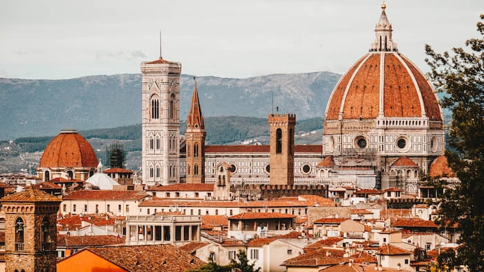 Tops Of Buildings In Florence, Italy With Mountain Range Behind