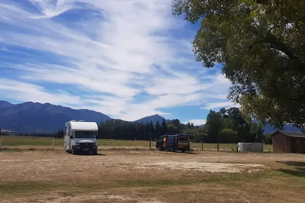 A landscape shot of a camper in the distance on a grassy field with mountains in the background.